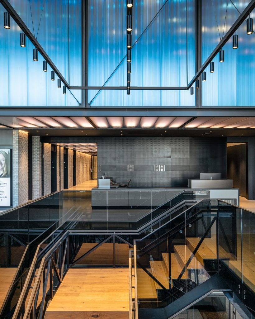 Alliance Bernstein 13 Sleek office lobby in Nashville, TN, with glass staircase, wood finishes, and an illuminated ceiling.