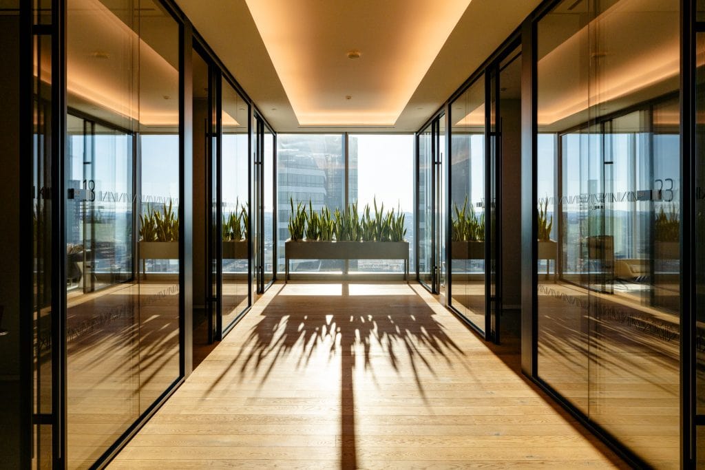 Alliance Bernstein 9 Sunlit hallway with wood flooring, indoor plants, and city views through glass walls.