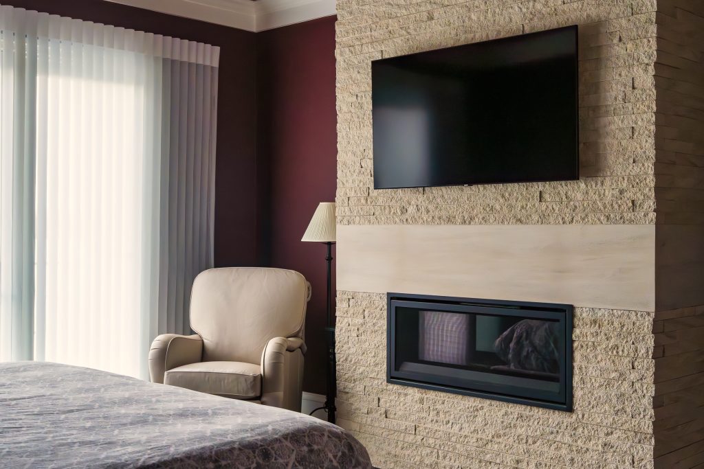 Crystal Lake 5 A cozy bedroom featuring a built-in fireplace with a stone accent wall and a mounted flat-screen TV. This warm and modern space invites relaxation and comfort with rich textures and thoughtful details.