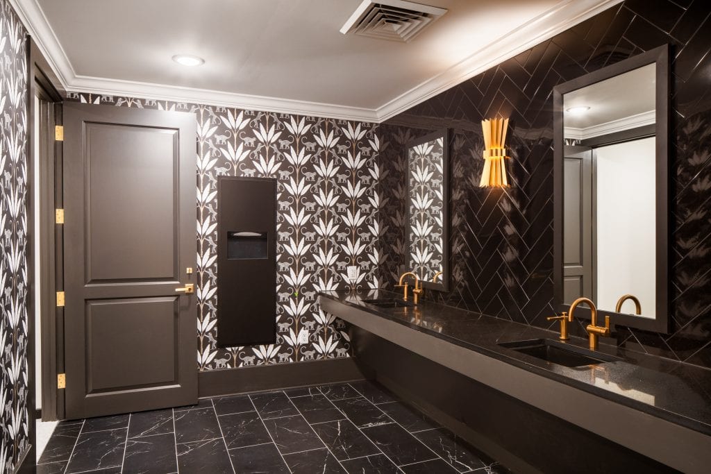 THE BOULEVARD 16 Modern bathroom with black and white tile, gold fixtures, and patterned wallpaper.
