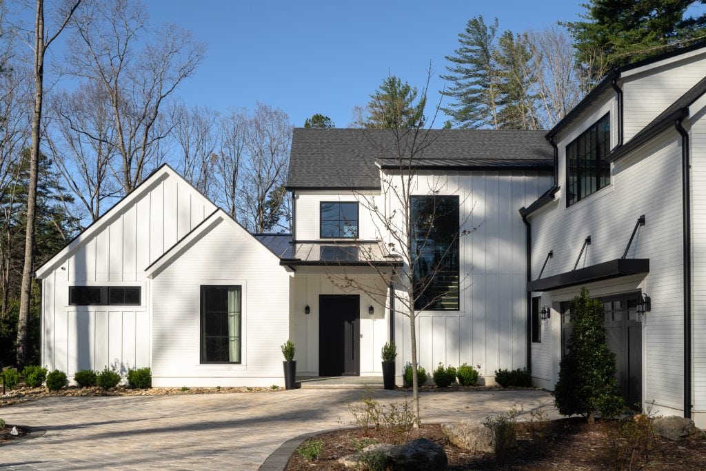 Flowering Vine 1 Front view of a modern white farmhouse with black accents and a spacious driveway.