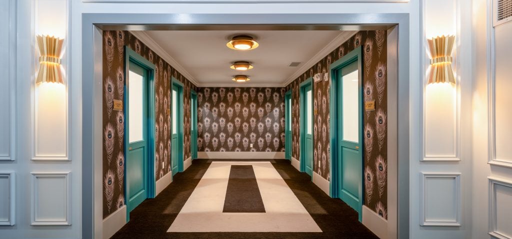 THE BOULEVARD 6 Elevator hallway with vibrant peacock wallpaper, colorful doors, and modern light fixtures.