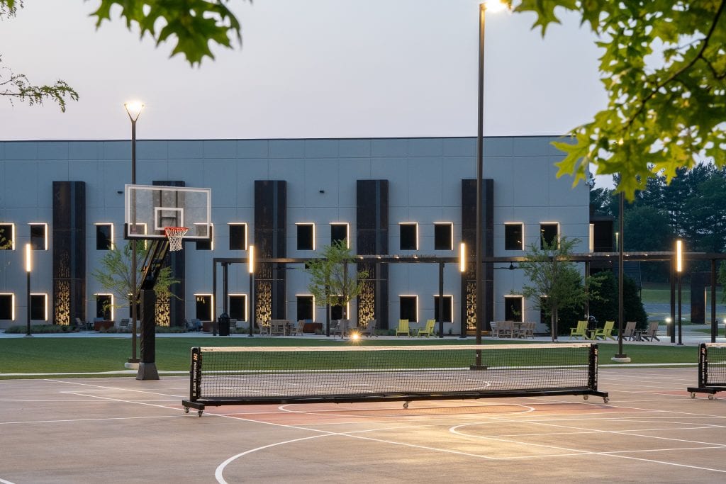 Long Hollow 4 Basketball court with modern illuminated building facade in the background.