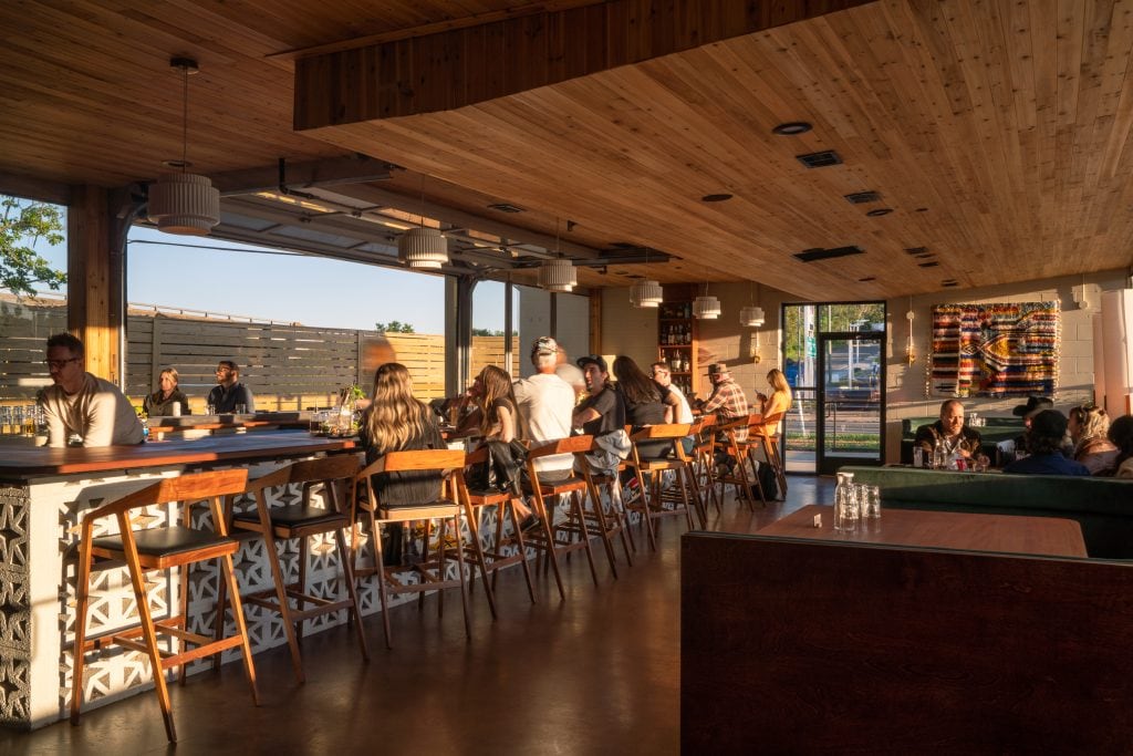 Golden Pony 12 Guests enjoying drinks at a stylish bar with warm wooden tones and pendant lights.