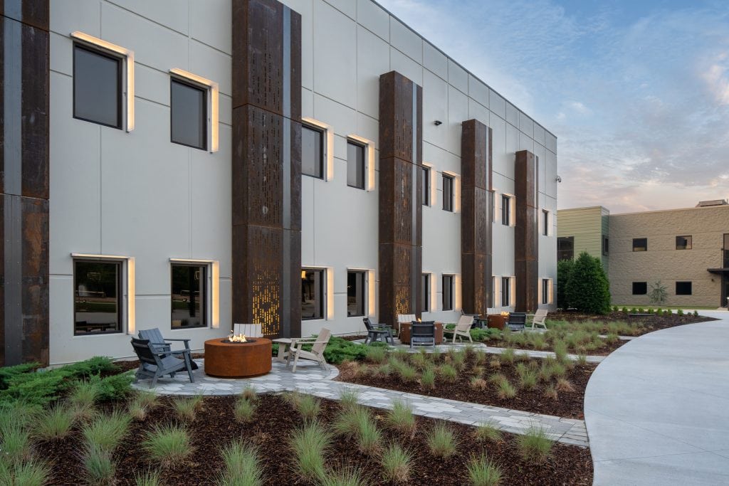 Long Hollow 6 Outdoor seating area with modern firepit, greenery, and warm lighting at dusk.