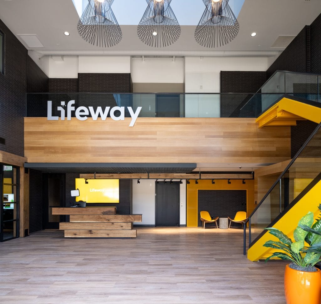 Lifeway 2 Spacious corporate lobby with wood finishes, a yellow staircase, and skylights.