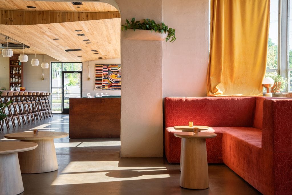 Golden Pony 10 Sunlit corner seating with red velvet booth, round wooden tables, and warm curtains.