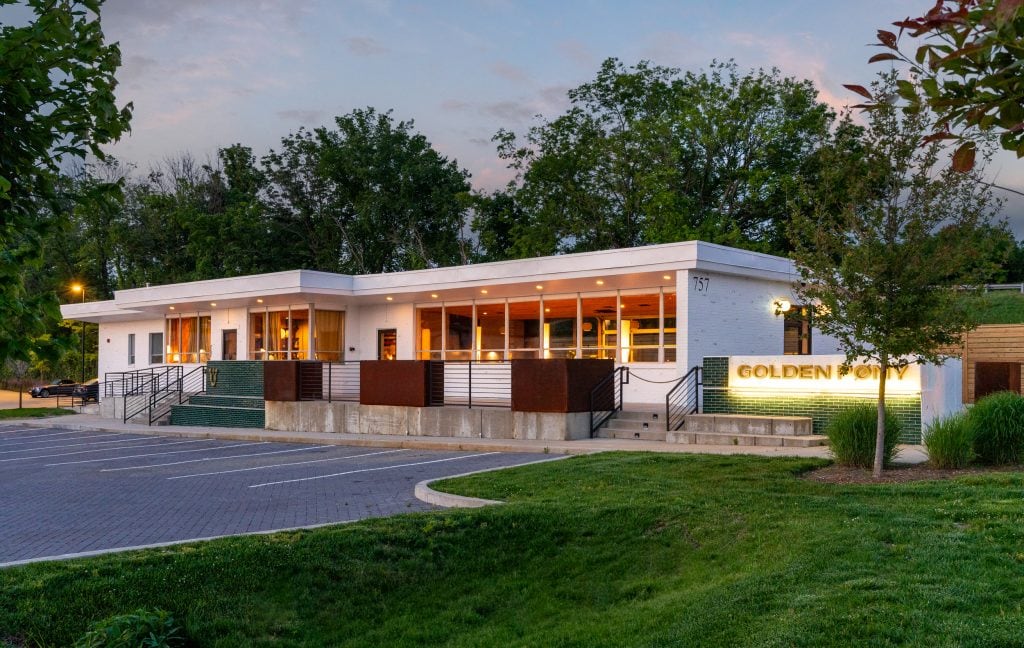 Golden Pony 21 Twilight view of Golden Pony building with soft ambient lighting and lush greenery.