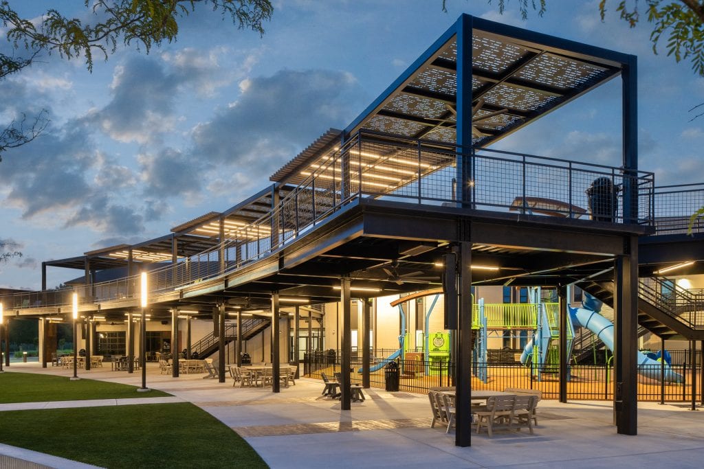 Long Hollow 3 Outdoor seating area with metal pergola and illuminated playground at dusk.