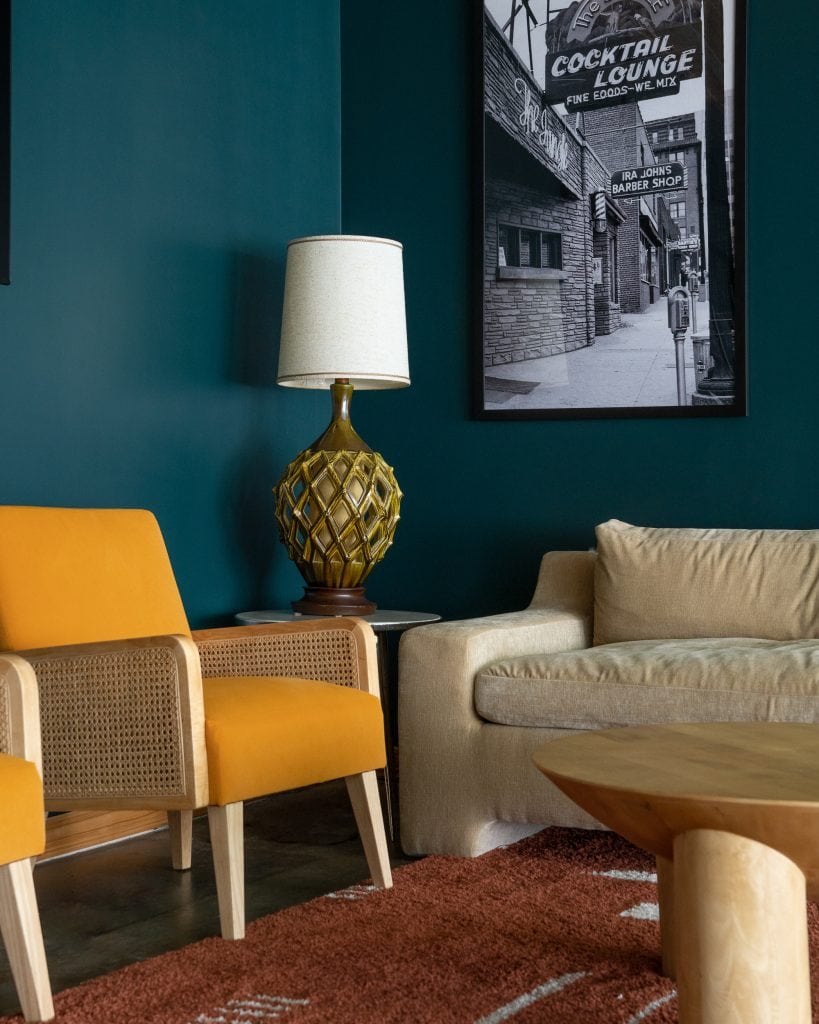 Golden Pony 6 Close-up of mustard rattan chair, vintage lamp, and framed black-and-white cocktail lounge print.