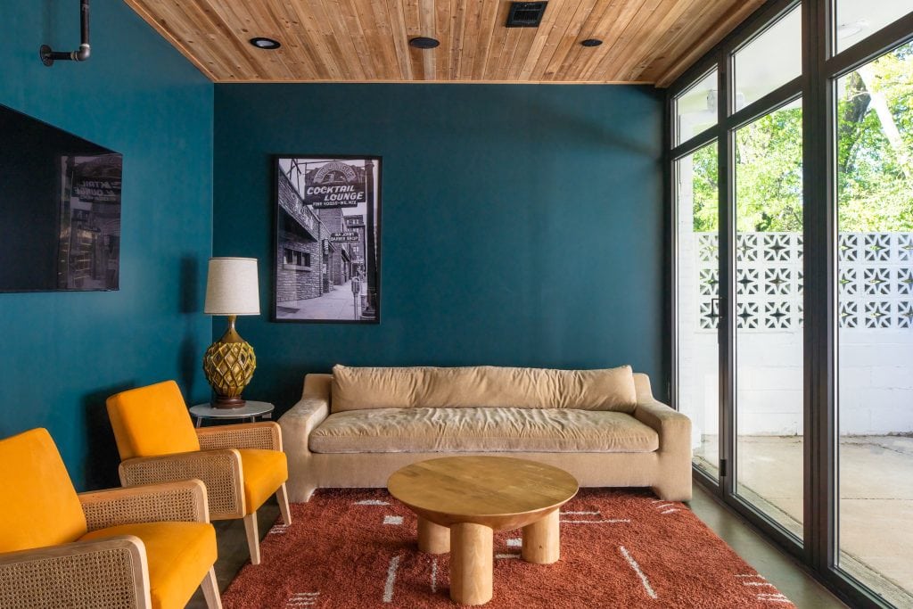 Golden Pony 5 Seating area with teal accent wall, vintage artwork, mustard chairs, and a beige sofa.