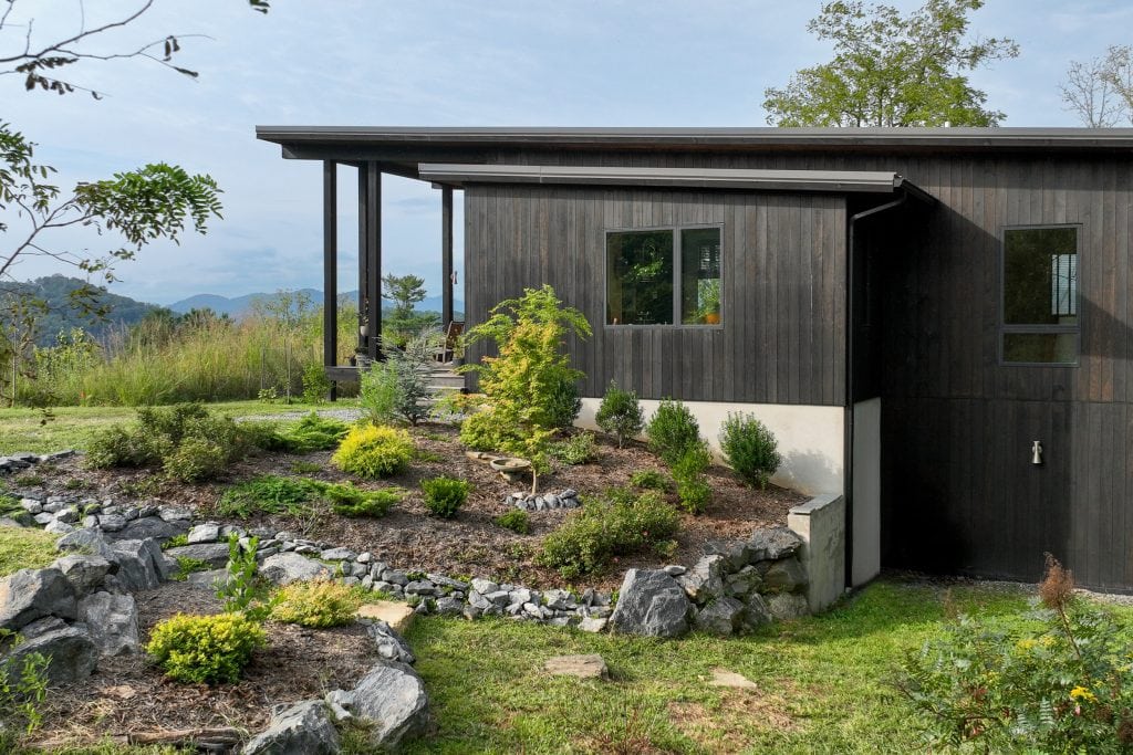 Freedom Cove 1 Black wood-clad modern home with large windows and lush landscaping.