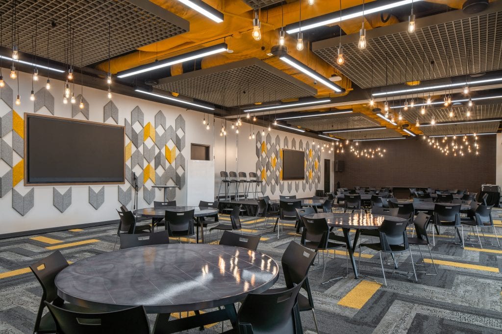 Lifeway 4 Spacious event hall with geometric wall panels, black chairs, and warm pendant lighting.