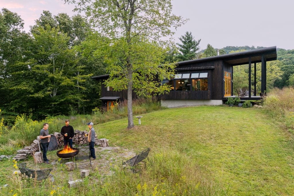 People gathered around a fire pit outside a modern home at dusk.