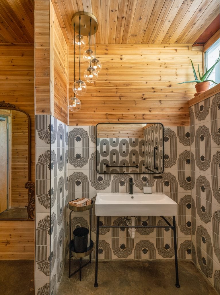 Golden Pony 8 Bathroom with geometric tile walls, wood-paneled ceiling, and globe pendant lighting.