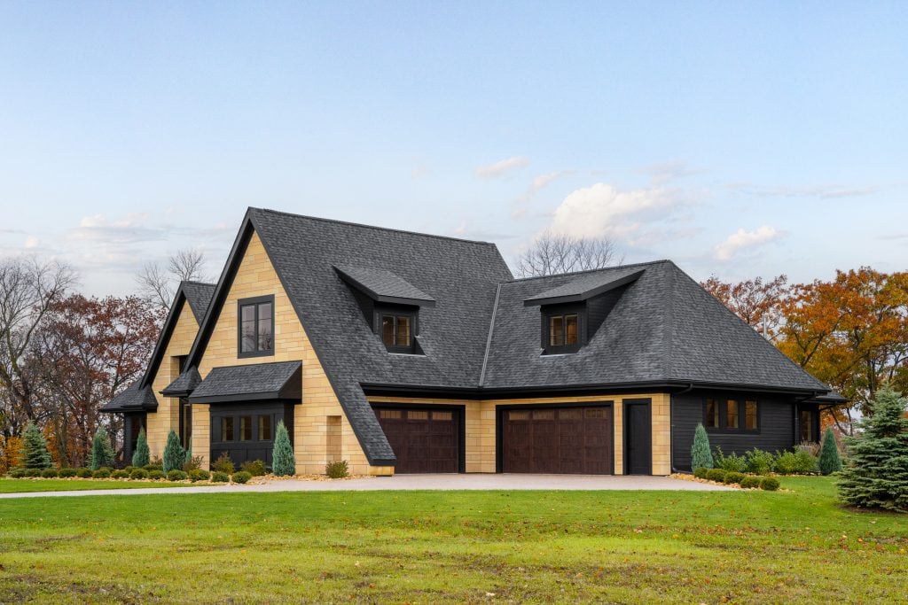 Marie 3 Angled view of a modern home with dark roofing, stone siding, and large windows.