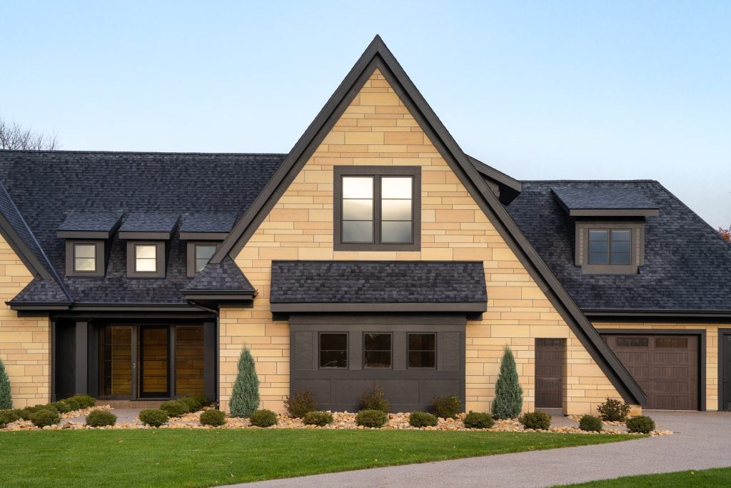 Marie 2 Close-up view of a modern home's front entrance with stone siding, black trim, and dormer windows.