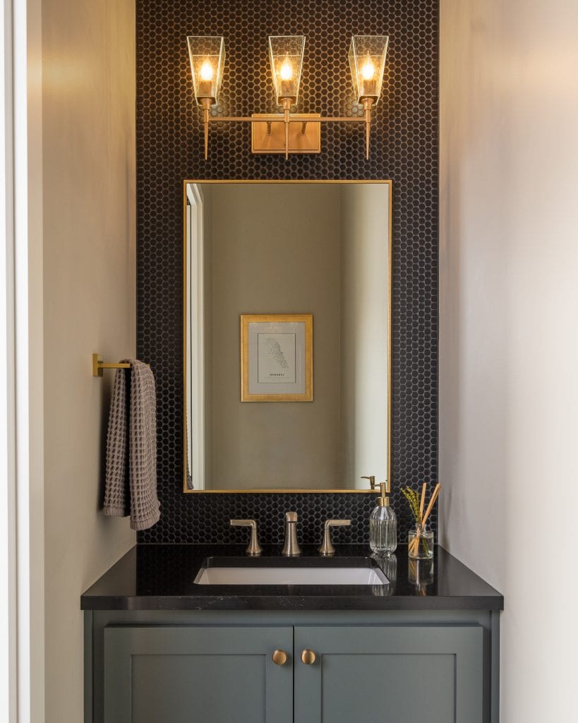 Marie 9 Modern powder room with dark hexagonal tile, gold light fixtures, and a black vanity.